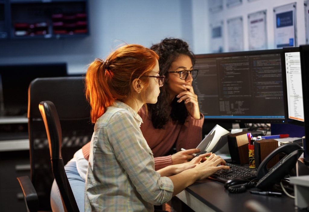 Two women wearing glasses are sitting down working on a computer