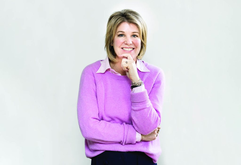 Jo Fisher stands in front of a grey background, her chin resting on her hand.