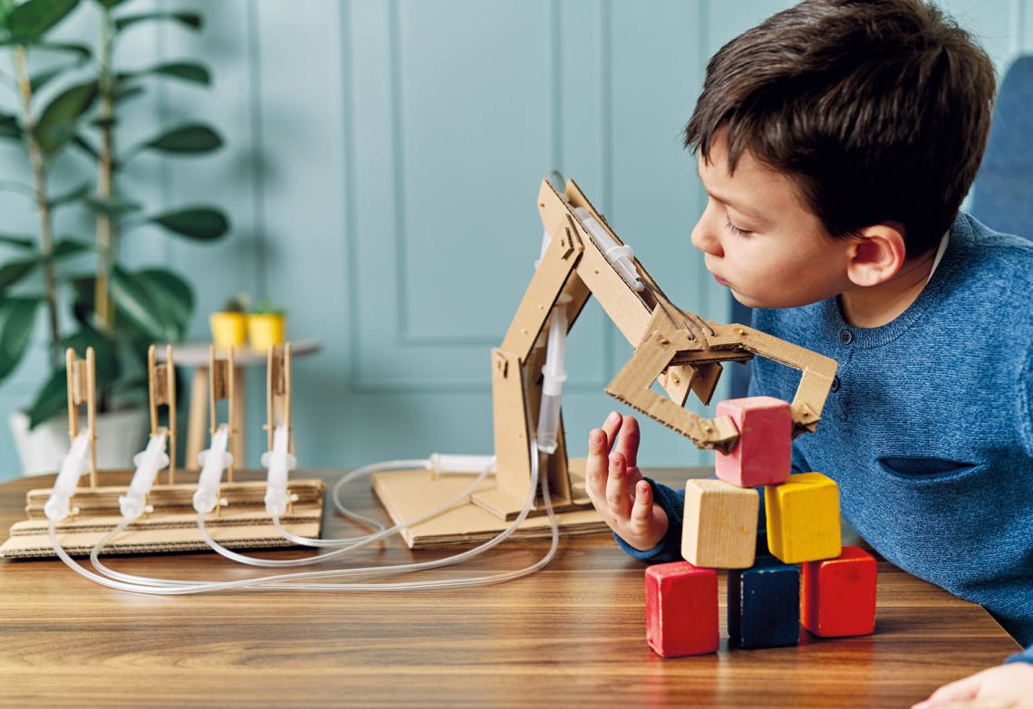 A boy looks at a robotic arm made of cardboard