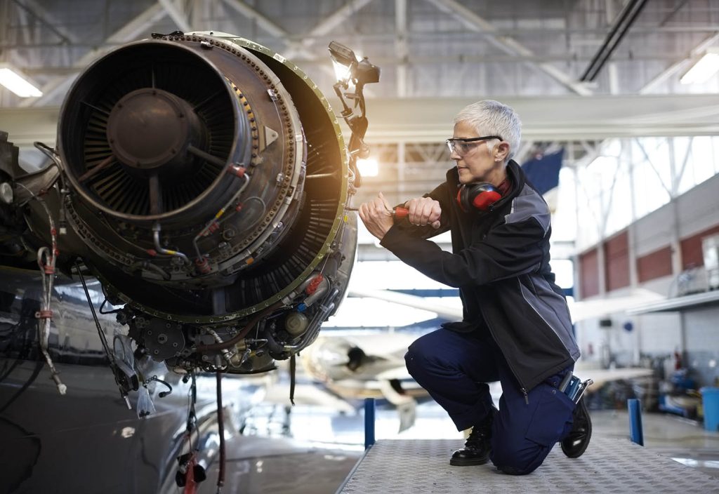 Senior female engineer in the hangar repairing and maintaining airplane jet engine.