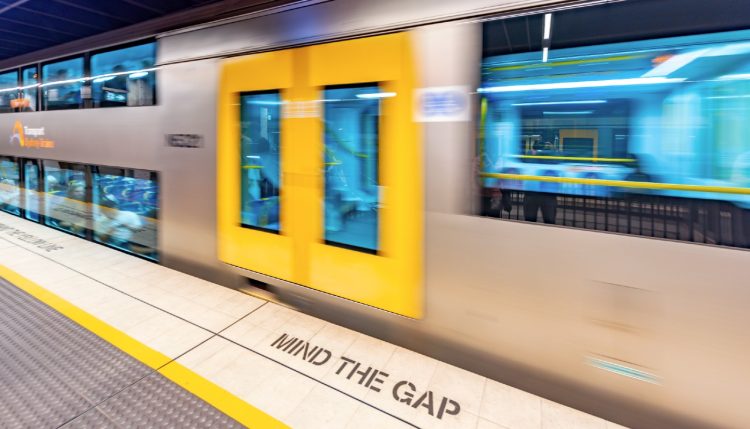 Moving train with 'Mind the Gap' written on the ground next to it.