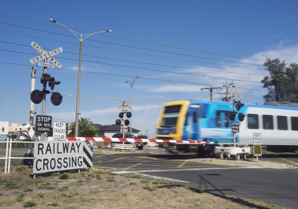 A commuter train passes through a railway level crossing on Eel Race Road, Seaford, Melbourne. Stock Photo