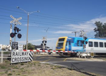 A commuter train passes through a railway level crossing on Eel Race Road, Seaford, Melbourne. Stock Photo