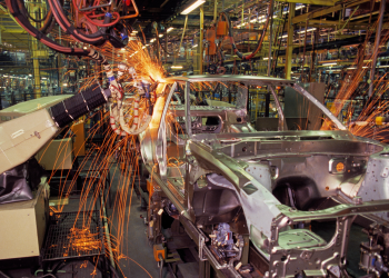 Sparks fly from a car chassis in a busy factory.